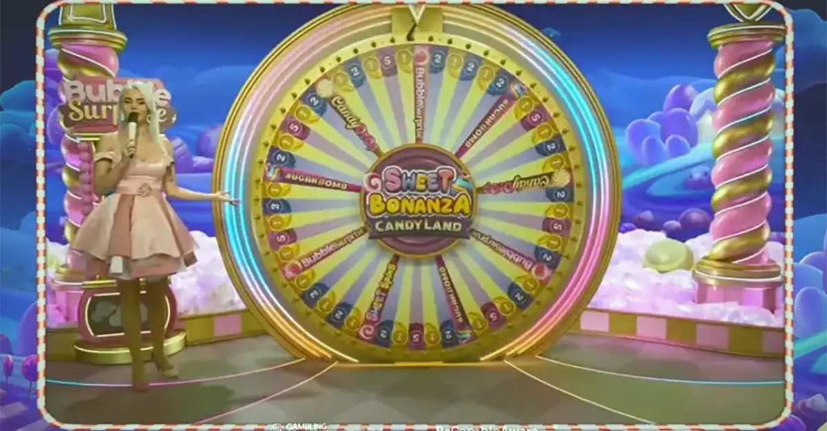 “Live game show host standing beside a large colorful bonus wheel in a candy-themed studio set for Sweet Bonanza CandyLand, with pastel clouds and bright decorations in the background.”
