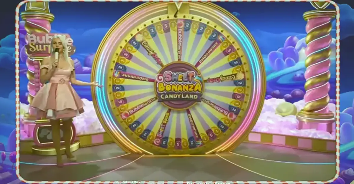 “Live game show host standing beside a large colorful bonus wheel in a candy-themed studio set for Sweet Bonanza CandyLand, with pastel clouds and bright decorations in the background.”
